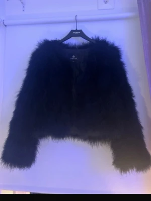 Svart fluffig pälsjacka från Chelsea - Säljer en svart, kort och superfluffig pälsjacka från Chelsea. Jackan har lång ärm och en riktigt mjuk, lurvig känsla som ger en cool och trendig look. Köpt på second hand. Använt en gång men passar inte mig i storleken egentligen. Säljer den på min Vinted också där är bilderna ifrån. Den har som klämmor som man kan stänga den där fram.