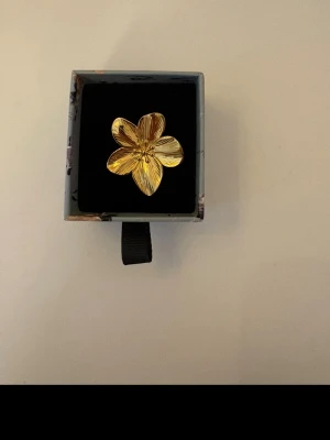 Guldfärgad blomring  - Snygg ring i guldfärgad metall med en stor blomformad detalj. Blomman har fem blad med fina räfflade detaljer som ger en cool och unik look. 