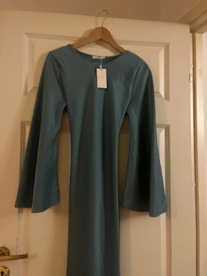 Blå långärmad klänning med snörning - Stilren blå klänning från NA-KD med långa utsvängda ärmar och snygg snörning i ryggen. Klänningen har en enkel, rak passform och är tillverkad i ett mjukt material som känns bekvämt mot huden. Den passar alla Imed att man kan knyta åt den i ryggen för ens egen kropp.