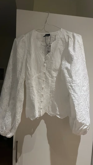 Vit blus med ballongärmar från Gina Tricot - Superfin vit blus från Gina Tricot med broderade blommor och ballongärmar. Blusen har knappar framtill och är gjord i ett lätt bomullstyg. Perfekt för dig som gillar romantisk och trendig stil med extra volym på ärmarna. Helt ny med lapp kvar, endast provad men den var för stor. Budgivning under priset som är satt🩷
