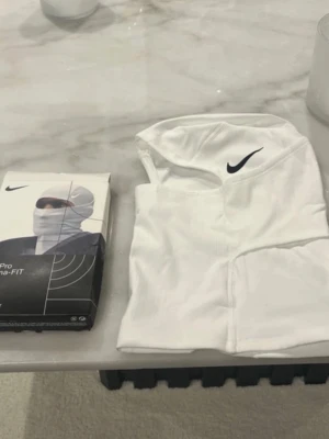 Vit Nike Pro balaclava Dri-FIT - Säljer en vit balaclava från Nike Pro med Dri-FIT-material. Den har en tight passform, svart Nike-logga framtill och är tillverkad i ett stretchigt funktionsmaterial som andas. Perfekt för träning utomhus eller kalla dagar.