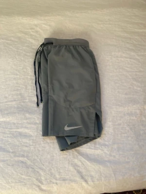 Grå träningsshorts från Nike - Snygga grå träningsshorts från Nike med elastisk midja och snörning. Shortsen har en sportig look med diskret Nike-logga framtill och är tillverkade i ett lätt och snabbtorkande polyestermaterial. Perfekta för gymmet eller löprundan. Pris kan diskuteras 