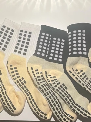 Randiga halksockor i svart och vitt - Säljer ett par halksockor med svart och vitt rutmönster på ovansidan och halkskydd under foten. Strumporna är ribbade och har en beige fotdel. Perfekta för att glida runt hemma utan att halka. 4st.