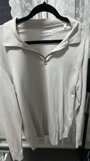 Beige ziptröja från These Glory Days - Snygg beige långärmad tröja från These Glory Days i mjuk bomull. Tröjan har en klassisk krage och dragkedja framtill för en avslappnad look. Perfekt för lager-på-lager och enkel att matcha med jeans eller chinos.