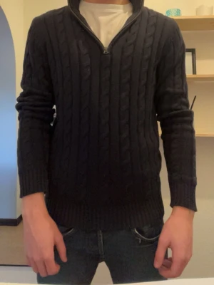 Mörkblå kabelstickad tröja GANT - Säljer en mörkblå kabelstickad  med halv dragkedja vid halsen. Tröjan har ribbade muddar och nederkant samt ett klassiskt kabelmönster. Perfekt för dig som gillar stilrena och tidlösa plagg perfekt skick 