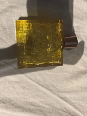 Versace gul parfymflaska - Snygg parfym från Versace i en fyrkantig, genomskinlig gul flaska med mönstrad yta och bronsfärgad kork. Flaskan har Versaces ikoniska Medusa-huvud ingraverat på framsidan och känns riktigt lyxig och modern. Köpte den för 1900 den är full har aldrig använt tycker den inte lukta gott. 