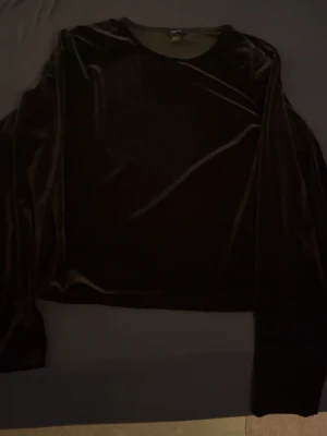 Svart sammets-tröja från Lindex - Mjuk och glansig svart tröja i sammet från Lindex. Tröjan har rund halsringning och långa ärmar, perfekt för dig som gillar en stilren och lite lyxig look. Passar till många olika outfits och är riktigt skön att bära.