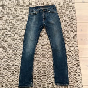 Blå slim fit jeans från Nudie Jeans - Snygga blå slim fit jeans från Nudie Jeans med klassisk femficksdesign och diskreta slitningar. Jeansen har smal passform, normal midja och är tillverkade i stretchigt denim för extra komfort. Perfekta för en avslappnad och trendig stil. Båda framfickorna är lite trasiga och det finns ett litet hål på baksidan, därav pris. Kan troligtvis sänka pris ytterligare lite så kom med förslag!!!
