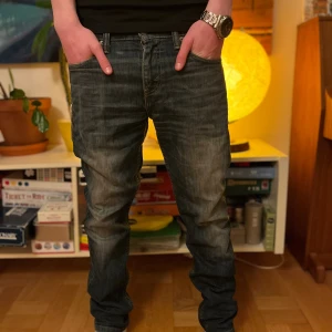 Levis jeans  - Säljer ett par mörkblå jeans med tvättad och lätt sliten look. Jeansen har rak passform, klassiska fem fickor och normal midja. Perfekta för dig som gillar en avslappnad stil med lite edge.