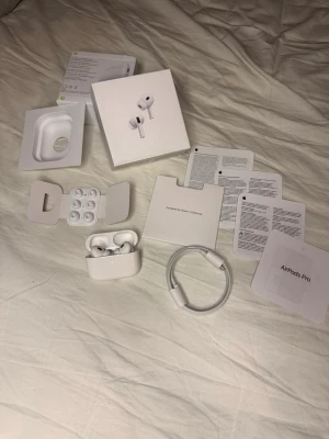 Apple AirPods Pro med laddningsetui - Säljer ett par Apple AirPods Pro med trådlöst laddningsetui. Kommer med originalförpackning, extra öronproppar och laddningskabel. Snygg och stilren design i vit färg, perfekt för musik och samtal.