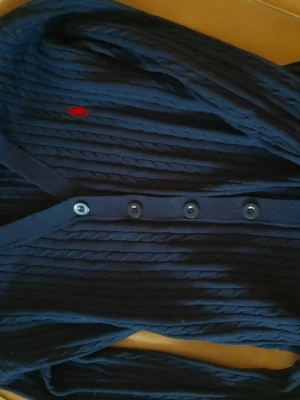 Mörkblå kabelstickad kofta Ralph Lauren  - Mörkblå kabelstickad kofta från Ralph Lauren med klassisk röd broderad logga på bröstet. Koftan har v-ringning, knäppning framtill med fyra knappar och ribbade muddar. Perfekt för lager-på-lager och snygg till jeans.(Är en discounted modell)priset är inte fast så pruta på!(Det är en doupe fast ser exakt likdan ut både med kvalite och logga)🤍