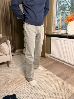 Gråa raka jeans från Woodbird  - Säljer ett par gråa jeans från Woodbird med klassisk femficksdesign och raka ben. Jeansen har en ljusgrå tvätt och normal passform, perfekt för dig som gillar en clean och avslappnad look. Materialet är robust denim och midjan är midwaist.