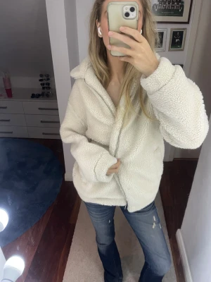 Vit teddyjacka med dragkedja - Mysig vit teddyjacka med stor krage och dragkedja framtill. Jackan har en loose passform och är tillverkad i fluffigt fleece-material som ger en chill och trendig vibe. Perfekt att slänga på sig när det är kallt ute. Snygg att styla med jeans eller leggings.