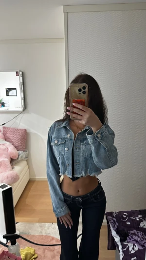 Croppad ljusblå jeansjacka - Säljer en croppad jeansjacka i ljusblå denim med rå, fransig nederkant. Jackan har klassisk krage, knappar framtill och två bröstfickor. Perfekt för dig som vill ha en trendig och edgy look.
