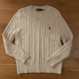 Vit kabelstickad tröja Polo Ralph Lauren - Säljer en ny vit kabelstickad tröja från Polo Ralph Lauren i storlek M passar även S. Tröjan har rund hals, ribbade muddar och det klassiska broderade Polo-logot på bröstet. Materialet: 30%Wool 35%Acrylic 35%Nylon. Fraktas inom 24 timmar efter köp.