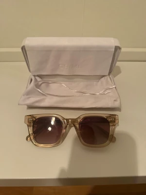 Beige fyrkantiga solglasögon från CHIMI - Snygga solglasögon från CHIMI med transparent beige båge och fyrkantig form. Glasen är mörka med en lätt tonad effekt. Kommer med originalfodral och mjuk påse. Perfekta för dig som vill ha en clean och modern look. Påsen är lite smutsig och snöret har tyvärr gått sönder men i övrigt så är allt super fint! Jag köpte de tidigare av en tjej på Plick men av mig har de inte används jättemycket ! Skirv till mig ifall ni vill ha fler bilder ! De är 04 med färgen Ecru 😍