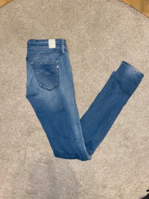 Replay LUZ jeans blå, storlek 29/32 - Snygga Replay LUZ jeans i klassisk blå tvätt med vita detaljer och diskret Replay-logga på fickan. Modellen har smal passform, normal midja och raka ben. Materialet är mjukt jeans-tyg i bomull med lite stretch för extra komfort.