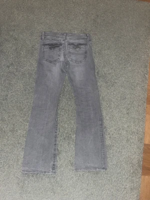 LOWWAIST Grå bootcut jeans med fickdetaljer - Snygga grå jeans med bootcut passform och coola fickdetaljer bak. Jeansen har klassisk femficksdesign, knappstängning och är tillverkade i mjukt jeanstyg. Perfekt för dig som gillar en avslappnad stil med lite edge. Man kan inte hitta dom i butik längre!