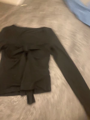 Svart långärmad topp med knyt - Svart långärmad topp med snygg knytning framtill och mjukt, stretchigt tyg. Rundad halsringning och figurnära passform som ger en clean och stilren look. Perfekt att matcha med jeans  eller kjol för en cool vibe. Jag är väldigt dålig på att ta bilder storlek xs men stretchig aldrig använt
