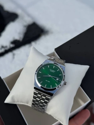 Silver - 500kr      Svart - 300kr - Casio Quartz klocka med stilren grön urtavla och datumvisning. Boetten är rund och har en polerad silverfärgad finish, medan armbandet är i klassisk länkdesign av metall. Klockan är vattentät upp till 50 meter och har minimalistiska indexmarkeringar.
