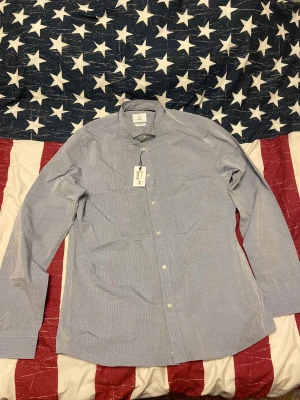 Ljusblå skjorta från Bläck XL - Snygg ljusblå skjorta från Bläck i storlek XL med diskret mönster och klassisk krage. Tailored fit för en modern siluett, knappar framtill och lätt struktur i tyget. Perfekt för dig som gillar stilrena detaljer och vill ha en skjorta som sticker ut lite extra. Skjortan är helt ny inte använd en ända gång. Nypris 699kr, mitt pris 300kr. Pris kan diskuteras. Storlek XL. 