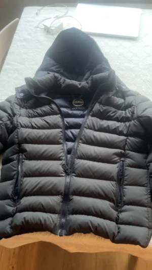 Svart pufferjacka från Colmar - Svart (grön i visst ljus) pufferjacka från Colmar Originals med huva och två sidofickor med dragkedja. Finns små defekter, (tråd har gått upp) fråga för bilder. Jackan har ett quiltat mönster och logotyp på ärmen. Perfekt för kalla dagar och har en snygg, modern look med normal passform. Priset kan gå ner.