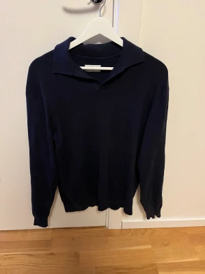 Marinblå pikétröja från These Glory Days - Snygg marinblå pikétröja från These Glory Days i storlek medium. Tröjan har klassisk krage och långärmad design, perfekt för dig som gillar stilrena och enkla plagg. Materialet är mjukt och stickat, vilket gör den skön att bära under kyligare dagar.