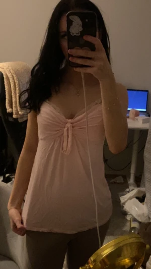 Vintage Ljusrosa linnetopp med spets och knyt - Supersöt ljusrosa linnetopp med spetsdetaljer vid halsringningen och en snygg knyt framtill. Toppen är ärmlös och har en mjuk, flowy passform som känns chill och feminin. Perfekt för dig som gillar romantiska vibes och pastellfärger. Den är från 2000 talet då jag har fått den av min mamma, Skulle nog säga storleken är S