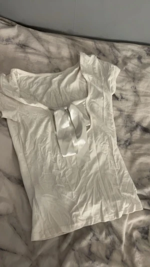 Vit blus med rosett på baksidan - Säljer en vit blus med korta ärmar och en snygg rosett på baksidan. Toppen har en mjuk och lätt känsla, perfekt för dig som gillar stilrena detaljer. Passformen är normal och materialet känns som bomull. Enkelt att matcha med dina favoritjeans eller kjol.