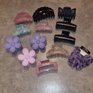 Mix av hårklämmor och scrunchies - Säljer ett färgglatt set med hårklämmor i olika former och färger, inklusive blommiga lila och rosa clips, glittrig klämma med pärlor, svarta klämmor med strass, samt lila scrunchies från SHEIN. Perfekt för att variera din frisyr med stil. 