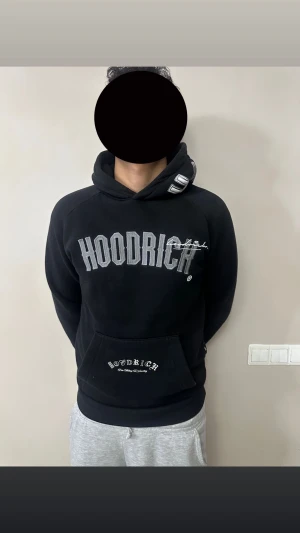 Svart HOODRICH hoodie med tryck - Svart hoodie från HOODRICH med stora broderade loggor på bröstet och huvan. Tryck även på fickan och ryggen. Klassisk känguruficka och huva med coola detaljer. Perfekt för dig som gillar streetwear och vill sticka ut.