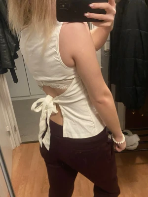 Vit omlottopp med knyt i ryggen - Säljer en vit omlottopp i bomull med snygg knytning i ryggen och öppen rygg. Toppen är ärmlös och har en clean, enkel design framtill. Perfekt för dig som gillar stilrena plagg med en twist på baksidan.