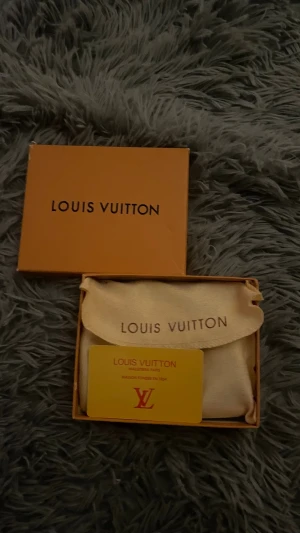 🔥NYÅRS RABBAT🔥Louis Vuitton rutig plånbok i skinn - Säljer en snygg svart rutig plånbok från Louis Vuitton med klassiskt Damier-mönster. Plånboken har guldfärgad dragkedja och flera fack för kort och sedlar. Kommer med original ask och dustbag. Perfekt för dig som gillar lyxiga accessoarer.
