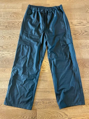 Rains Regnbyxor - Rains "Cargo Rain Pants Wide" regnbyxor. Svarta, i storlek S. Sparsamt använda, i jättefint skick. Originalkvitto medföljer. Säljs pga minskad användning. Bara att höra av dig vid intresse, frågor eller önskan om fler bilder!