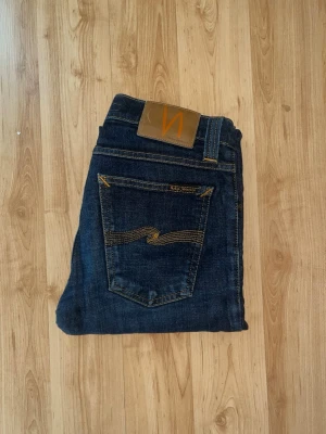 Nudie Jeans  - Säljer ett par mörkblå skinny jeans från Nudie Jeans i modellen Tight Long John. Jeansen är tillverkade i slitstarkt bomullsmaterial och har en smal passform. Midja 32cm, längd 102cm. JAG SKICKAR EJ FLER BILDER NÄR JAG BÄR JEANSEN! för bättre inblick i passformen rekommenderar jag att googla på modellnamnet. För storleksguide kolla måtten noggrant då jeansen alltid kan vara uppsydda heller krympta och jag ej tar emot returer :) s5,3
