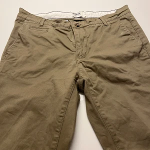 Beige chinos från Dobber - Snygga beige chinos från Dobber med klassisk rak passform och normal midja. Byxorna har fickor fram och bak, bälteshällor och stängs med knapp och dragkedja. Perfekta för en chill och stilren look. Materialet är mjuk bomull som känns skönt mot huden.