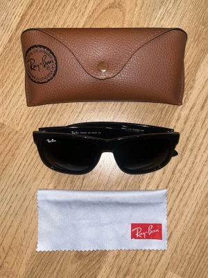 Svart Ray-Ban Wayfarer RB4165 - Säljer ett par klassiska svarta Ray-Ban Wayfarer RB4165 solglasögon. Snygg och tidlös modell med svart båge och mörka glas. Kommer med originalfodral i brunt läder och putsduk med Ray-Ban-logga. Perfekt accessoar för soliga dagar!