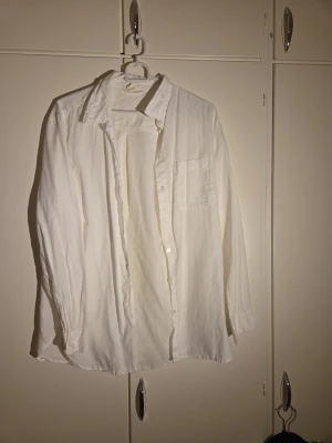 Vit bomullsskjorta med knappar - Vit skjorta i 100% bomull med klassisk krage och knappstängning framtill. Har en bröstficka och långa ärmar med manschett. Perfekt för en clean och chill stil, lätt att matcha med jeans eller kjol.