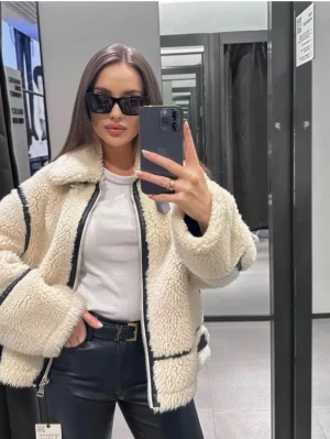 Beige/vit teddyjacka med svarta detaljer - Säljer en fluffig vit teddyjacka med svarta kantdetaljer och dragkedja framtill. Jackan är utan ”skärp detaljerna” som när jag köpte den fanns vid jackans sida och hals. I superfint skick och endast använd några få gånger!💗