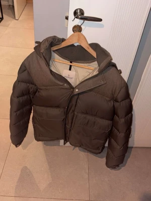 Moncler montegenevere - Säljer en mörkbrun pufferjacka från Moncler med två stora fickor framtill, huva och dragkedja. Jackan har en schysst mix av material med både polyester och ull, samt ribbad krage. Perfekt för dig som vill ha en varm och snygg jacka med cool design. Jackan är i gottskick förutom en väldigt liten skada på vänster armen som visas i bilden. Jackan är inköpt vintern 2024 för 22999 på nk i Stockholm. Priser kan diskuteras. Kontakta för information samt fler specificerade bilder