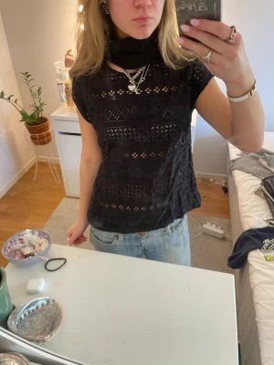 Svart spetsblus med kort ärm - Säljer en svart blus i spets med korta ärmar och snygga hålmönster. Toppen är lätt transparent och har en rak passform som är enkel att styla till jeans eller kjol. Perfekt för dig som gillar detaljer och vill ha en cool men feminin look.