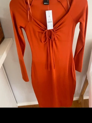 Orange långärmad klänning Gina Tricot - Snygg orange klänning från Gina Tricot i storlek XS. Modellen är figurnära med lång ärm och har en v-ringad hals med snörning framtill. Klänningen är mellanlång och tillverkad i mjukt stretchigt material som sitter bekvämt mot kroppen. Väldigt smickrande! 