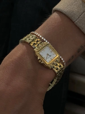 Guldfärgad fyrkantig klocka från Muli Collection - Snygg guldfärgad klocka från Muli Collection med fyrkantig urtavla och romerska siffror. Länken är i metall med polerad finish och klockan har en klassisk, stilren look. Urtavlan är vit med subtila detaljer och passar perfekt för dig som gillar tidlös design. Endast använd en gång. Nypris 1799kr 