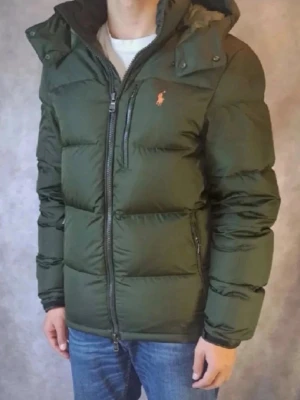 Polo Ralph Lauren Puffer Jacka  - Säljer en fet Army Green pufferjacka från Polo Ralph Lauren med huva och orange broderad logga på bröstet. Jackan är storlek M och är perfekt nu under de kyliga dagarna, Jackan är i bra skick med inga skador eftersom den är knappt använd! Priset går såklart att diskuteras!