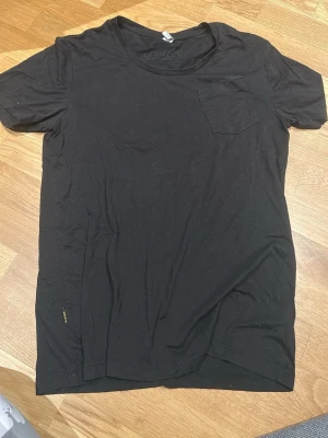 Svart t-shirt från G-Star RAW - Svart t-shirt från G-Star RAW med rund hals och liten bröstficka. T-shirten har korta ärmar och en diskret logga broderad vid fickan samt en liten G-Star RAW-tag på sidan. Materialet är mjuk bomull, perfekt för en chill och stilren look.