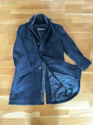 Herno - Säljer en stilren mörkblå rock från Herno med klassisk krage och knäppning framtill. Jackan har ett quiltat innerfoder och är tillverkad i ullblandning med detaljer i polyester. Perfekt för dig som vill ha en snygg och tidlös look under höst och vinter. Storlek S (48)