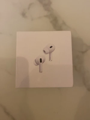 AirPods Pro - Säljer ett par Apple AirPods Pro i originalförpackning. Trådlösa hörlurar med aktiv brusreducering, transparensläge och hög ljudkvalitet. Kompatibla med iOS, iPadOS, Mac och Apple Watch. Kartongen ser ut att vara i nyskick utan synligt slitage.