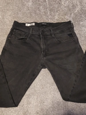 Replay Anbass svarta jeans - Svarta Replay Anbass jeans med klassisk femficksdesign och smal passform. Jeansen har en snygg mörk tvätt, svarta sömmar och en diskret Replay-logga på bakfickan. Materialet är stretchigt jeans för extra komfort och rörelsefrihet.