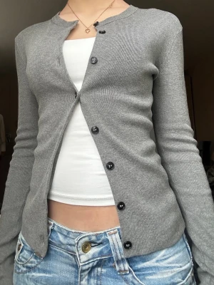 Grå kofta med svarta knappar - En jättesnygg grå cardigan/kofta med svarta knappar som lägger sig längs kroppen. Endast använd en gång, är köpt på H&M och har storleken xs💗💗