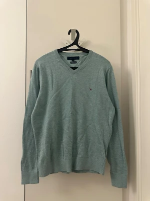 Ljusblå v-ringad tröja Tommy Hilfiger - Snygg ljusblå v-ringad tröja från Tommy Hilfiger i 100% bomull. Klassisk passform med diskret logga broderad på bröstet och ribbade muddar vid ärmslut och nederkant. Perfekt till lager på lager under höst och vår. 